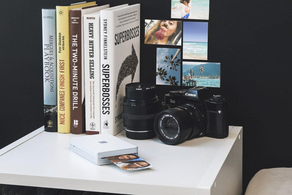 Lifeprint printer printing photo, with books and camera behind - Lifeprint photo printer for iPhone and Android